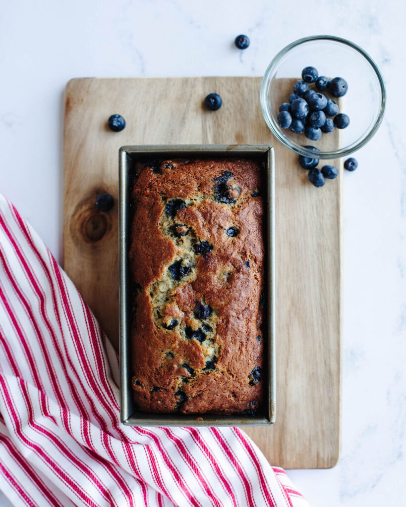 a loaf of Blueberry Banana Bread cooling in a loaf pan.