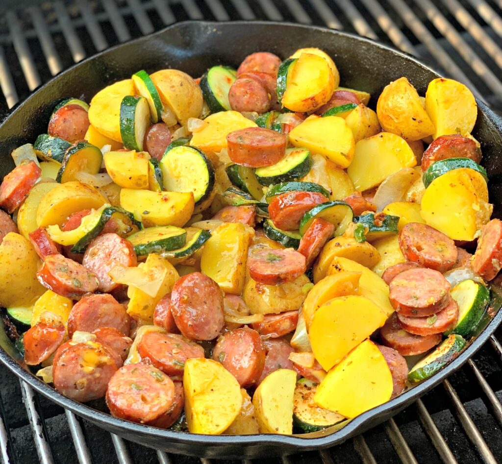a cast iron skillet with smoked sausage, potatoes, and zucchini slices