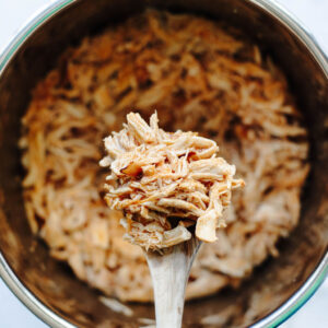 a wooden spoon scooping out some shredded cooked chicken seasoned with buffalo sauce.