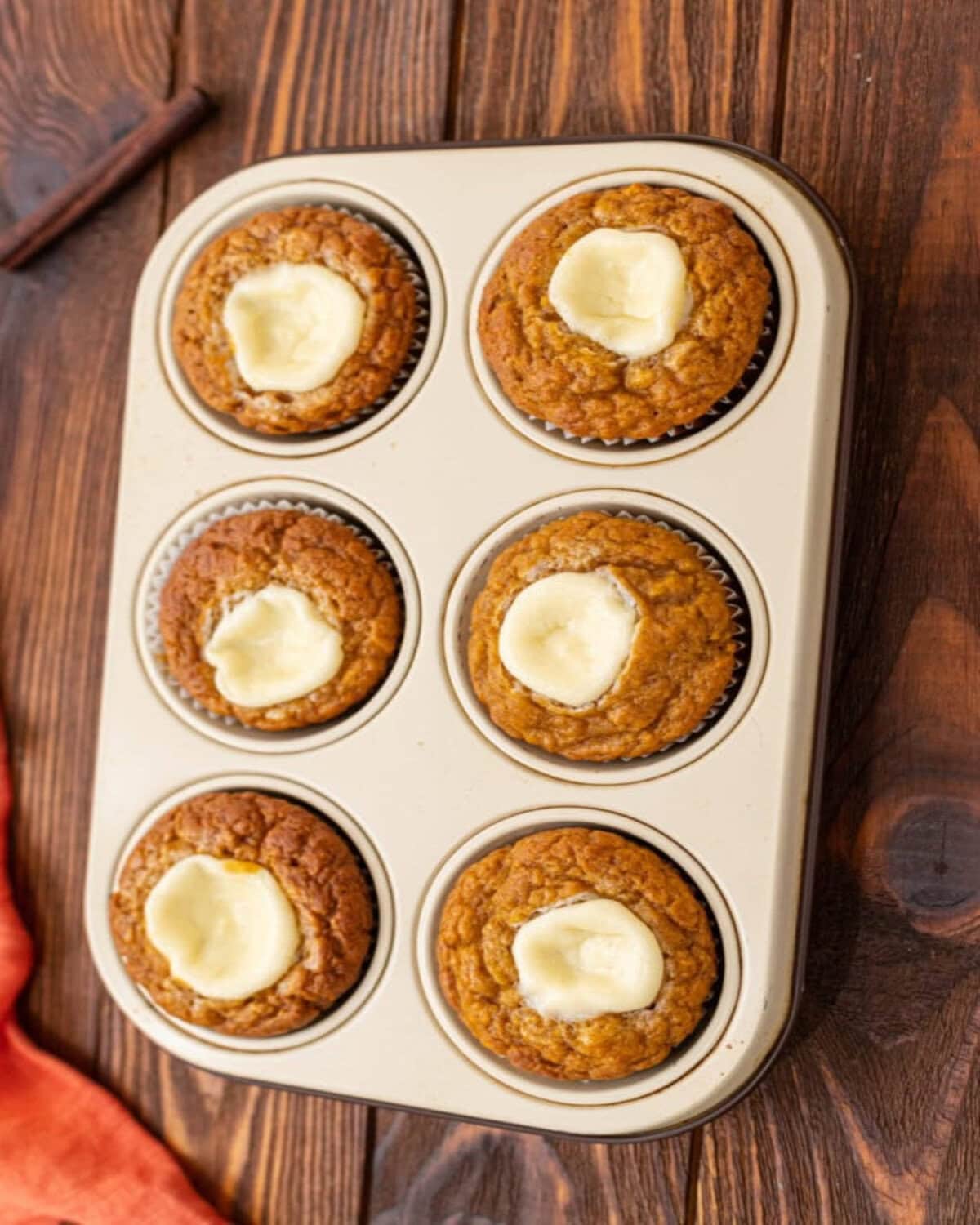 pumpkin muffins baked with a cream cheese center in a muffin pan and ready to serve.