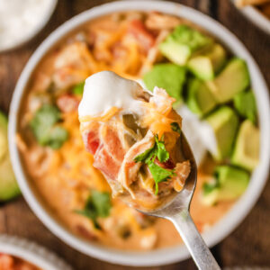 A spoon taking a scoop of soup from a loaded bowl.