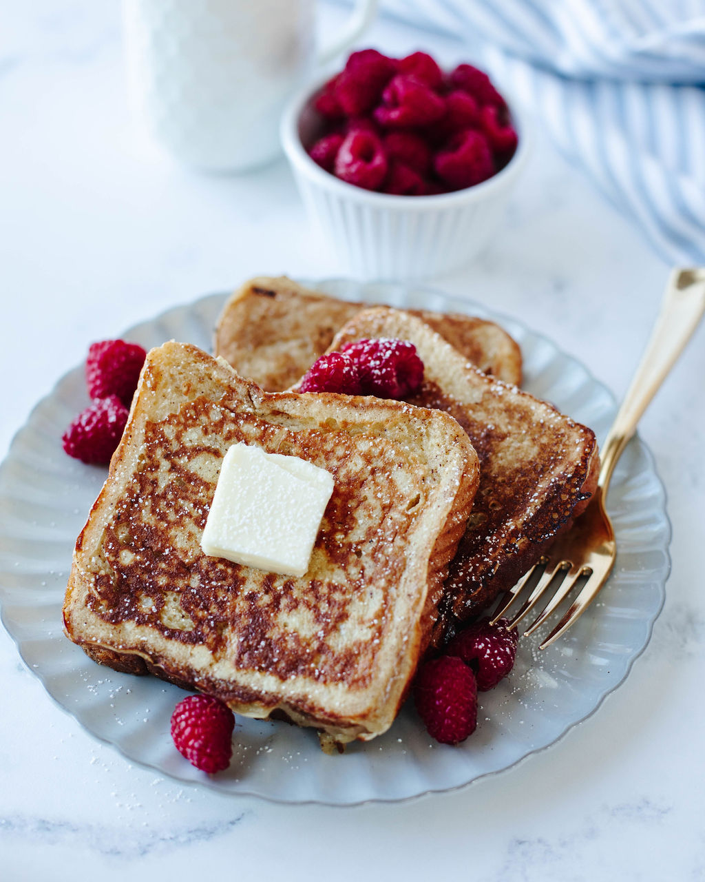 french toast topped with butter and raspberries on a white plate.