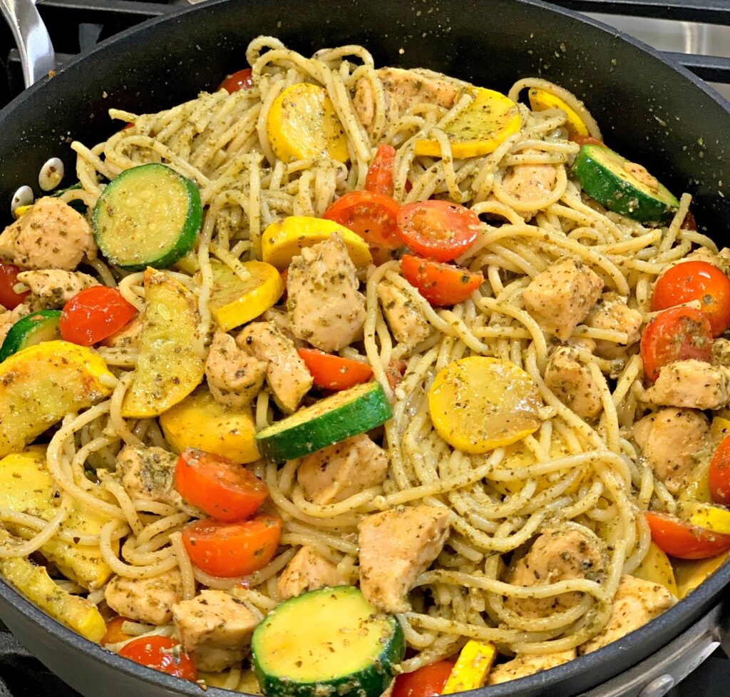 pesto sauce coating tender noodles with chicken, tomatoes, zucchini, and squash in a skillet