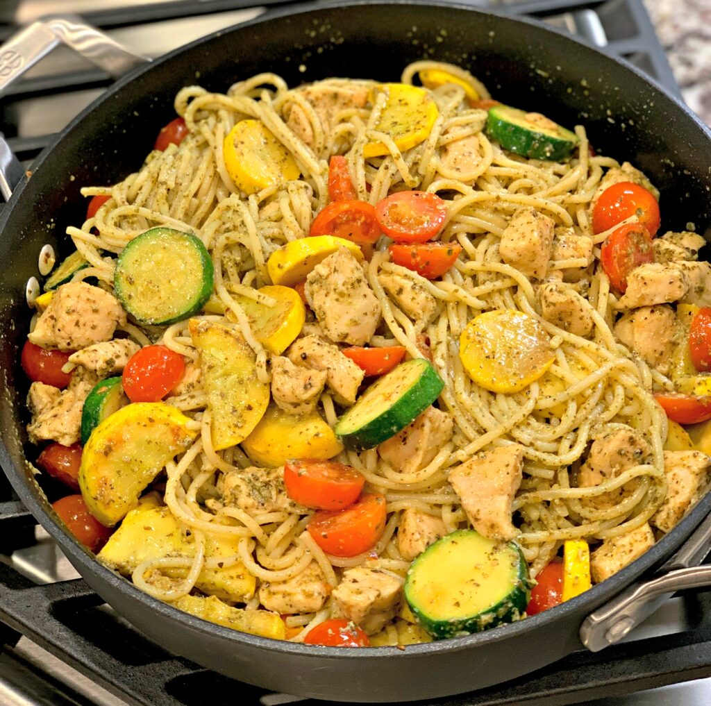a one pan skillet with pesto pasta, chicken, and vegetables
