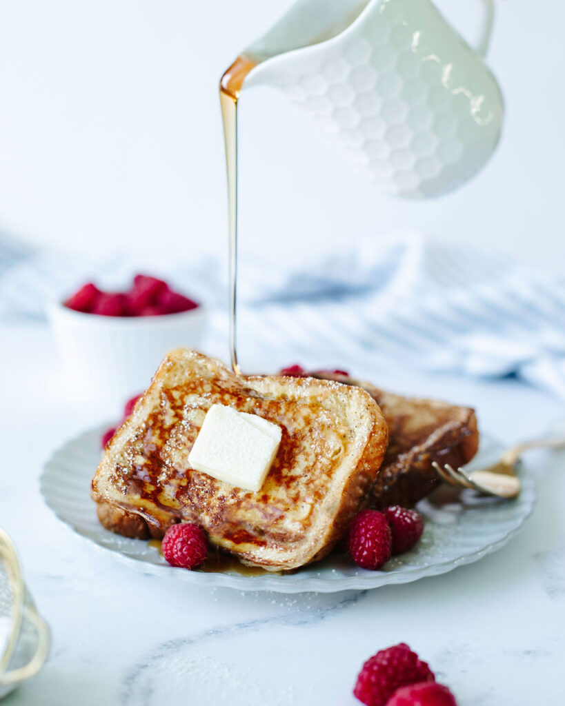 syrup being poured onto a white plate of french toast.