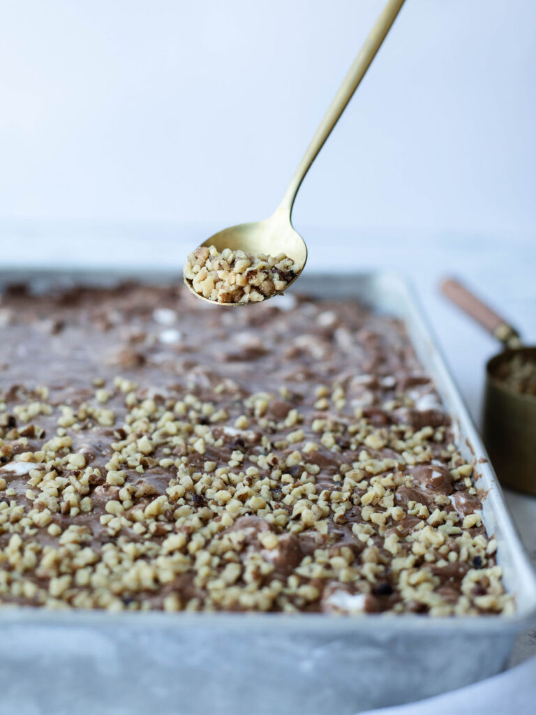 chopped pecans being sprinkled on top of a chocolate cake.