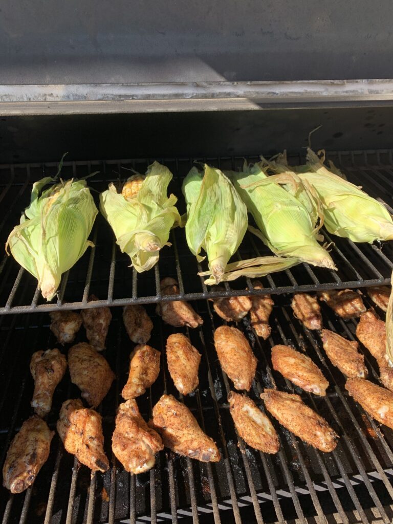 chicken wings and corn on the cob lined up on a smoker