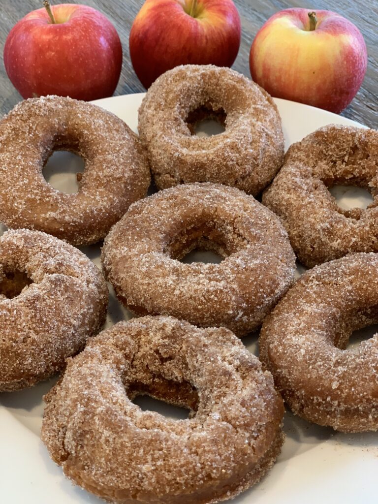 apple cider donuts lined on a plate with apples behind it