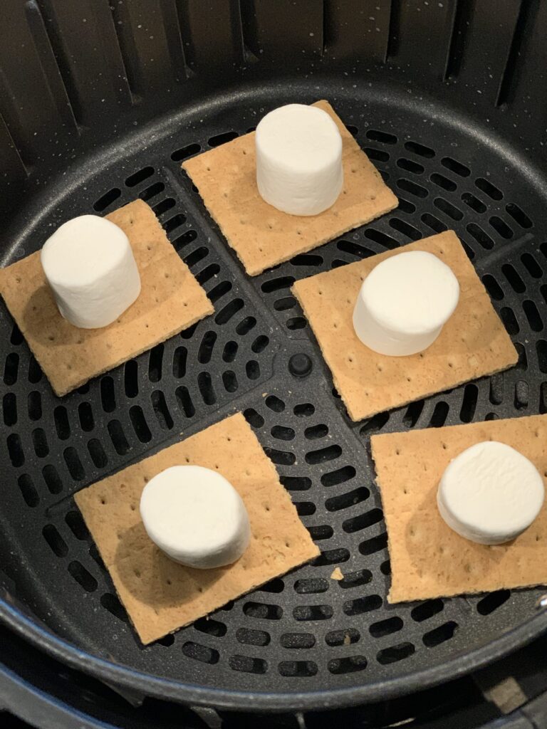 a marshmallow on top of a graham cracker lined up on the bottom of an air fryer