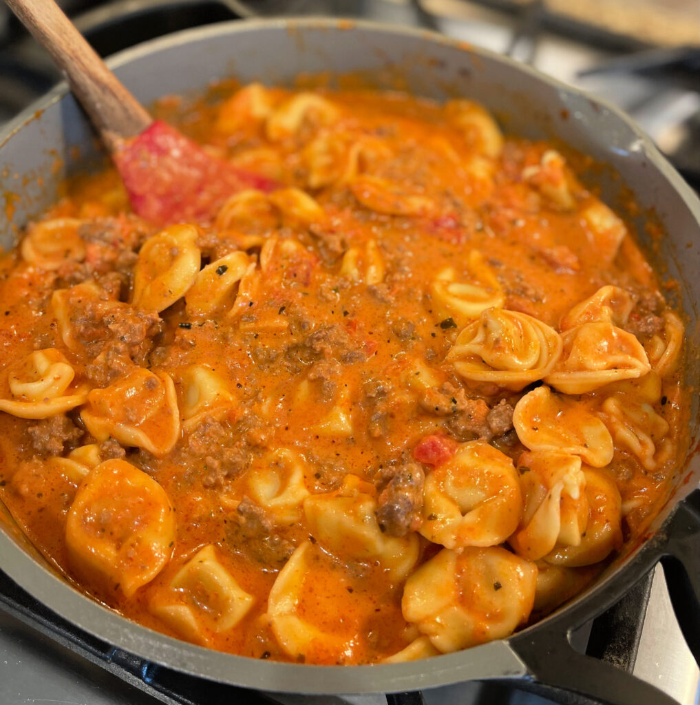 pasta sauce combined with tortellini and meat in a skillet
