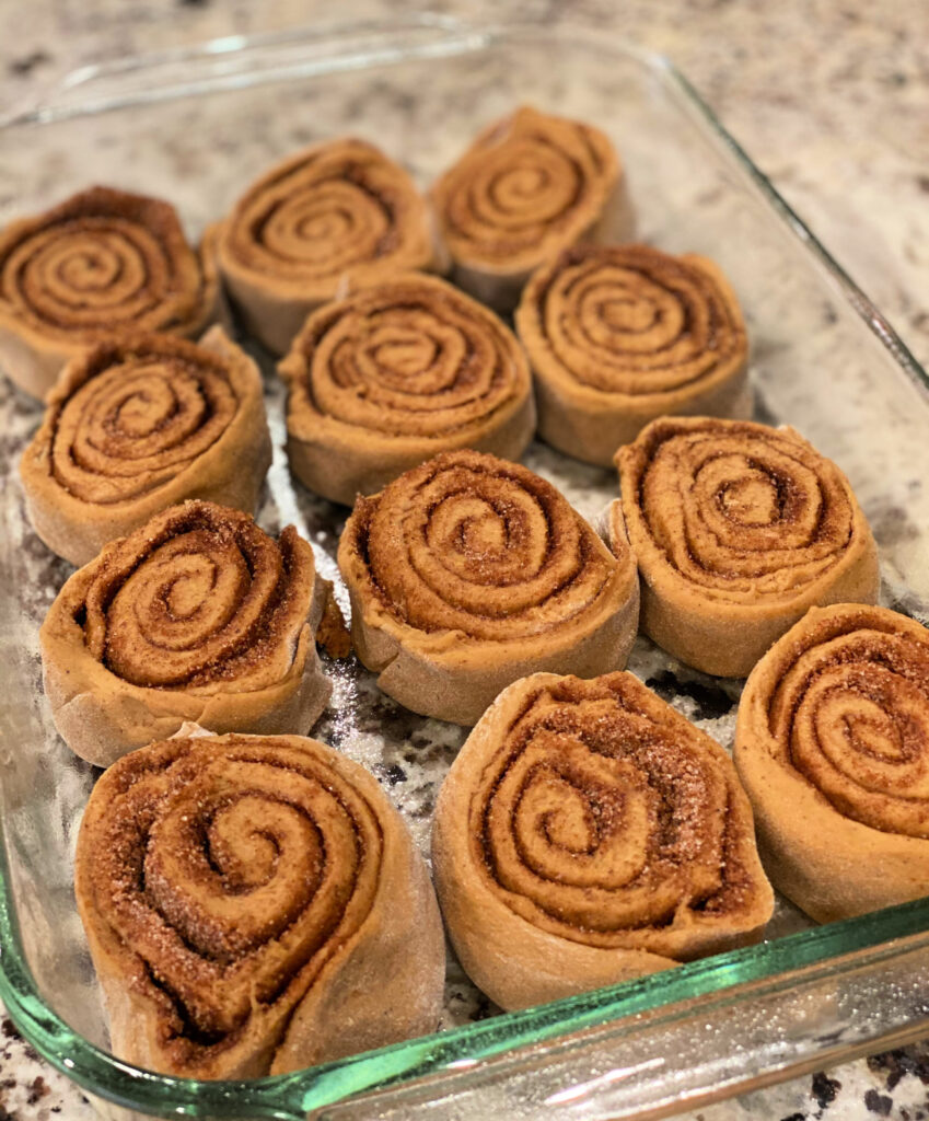 homemade cinnamon rolls lined up in a baking pan ready for the oven