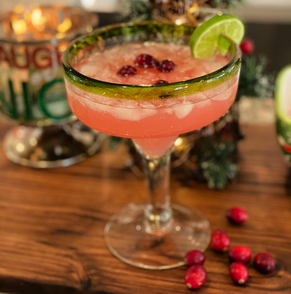cranberry margarita in a margarita glass garnished with a lime wedge and fresh cranberries