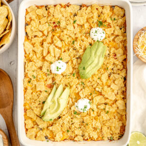 a cooked casserole topped with crushed tortilla chips and avocado.