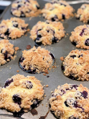 crumb topped streusel blueberry muffins in a baking mufifn pan.