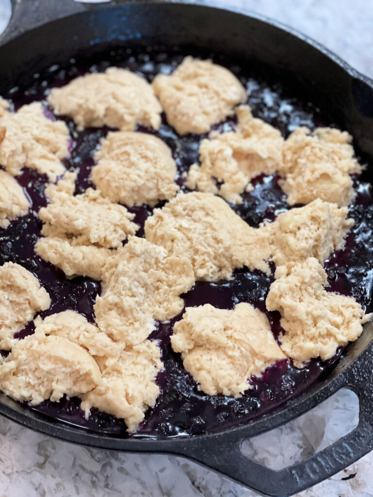 drops of biscuit mix over blueberries in a skillet