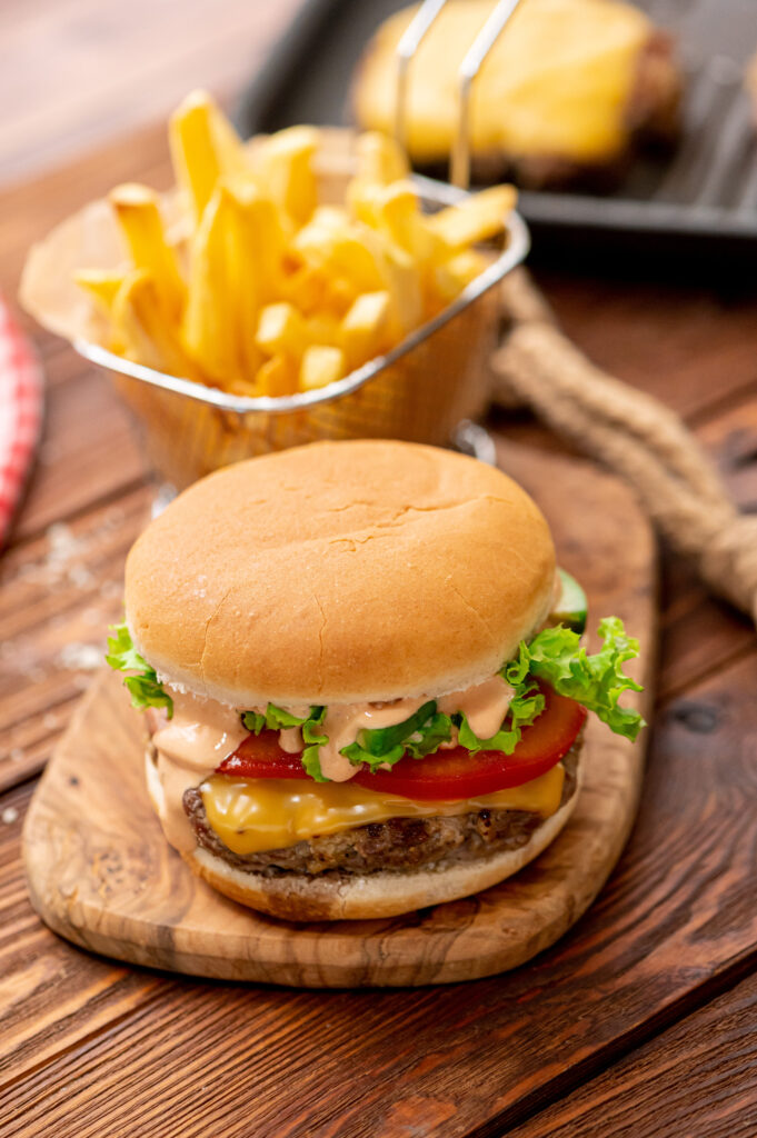 a juicy hamburger with fries behind it ready to enjoy.