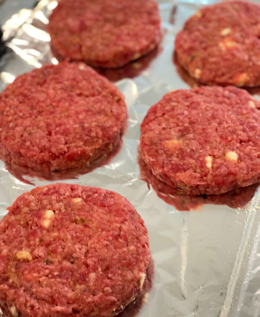 ground beef hamburger patties with toppings added in and ready to grill.