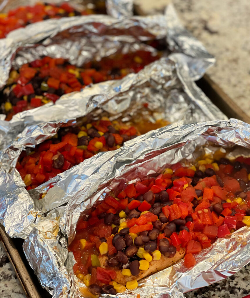 grilled fiesta chicken foil packets with tons of tomatoes, corn, beans, and more over chicken