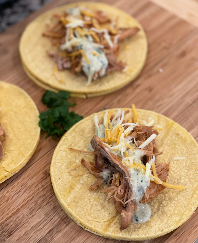 shredded pork on a taco shell with a creamy cilantro lime sauce drizzled