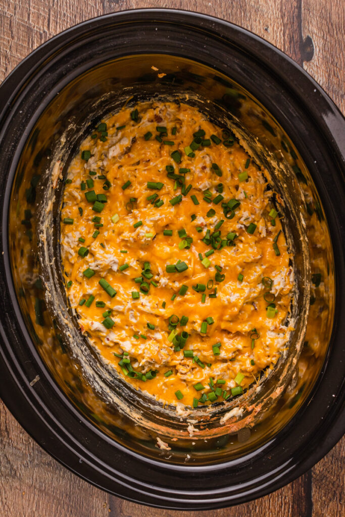 melted cheese and green onions over shredded chicken in a slow cooker