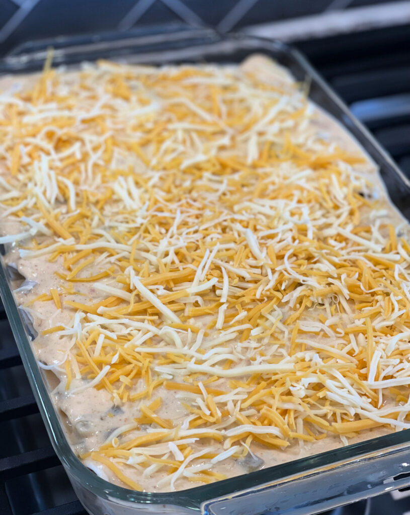 Shredded cheese on top of creamy enchiladas, ready for the oven.