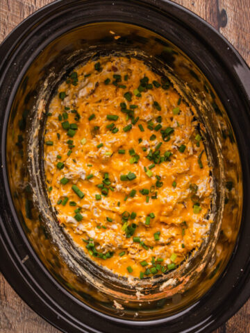 melted cheese and green onions over shredded chicken in a slow cooker