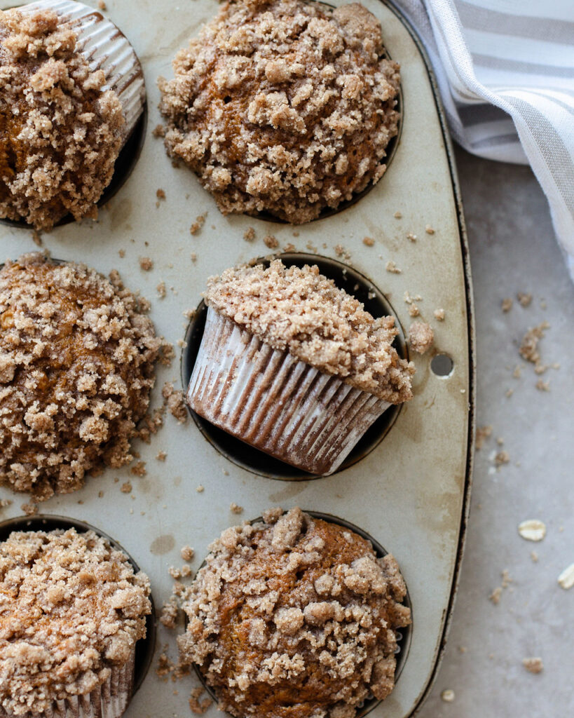 a crumb topped muffin on its side in a muffin tin.