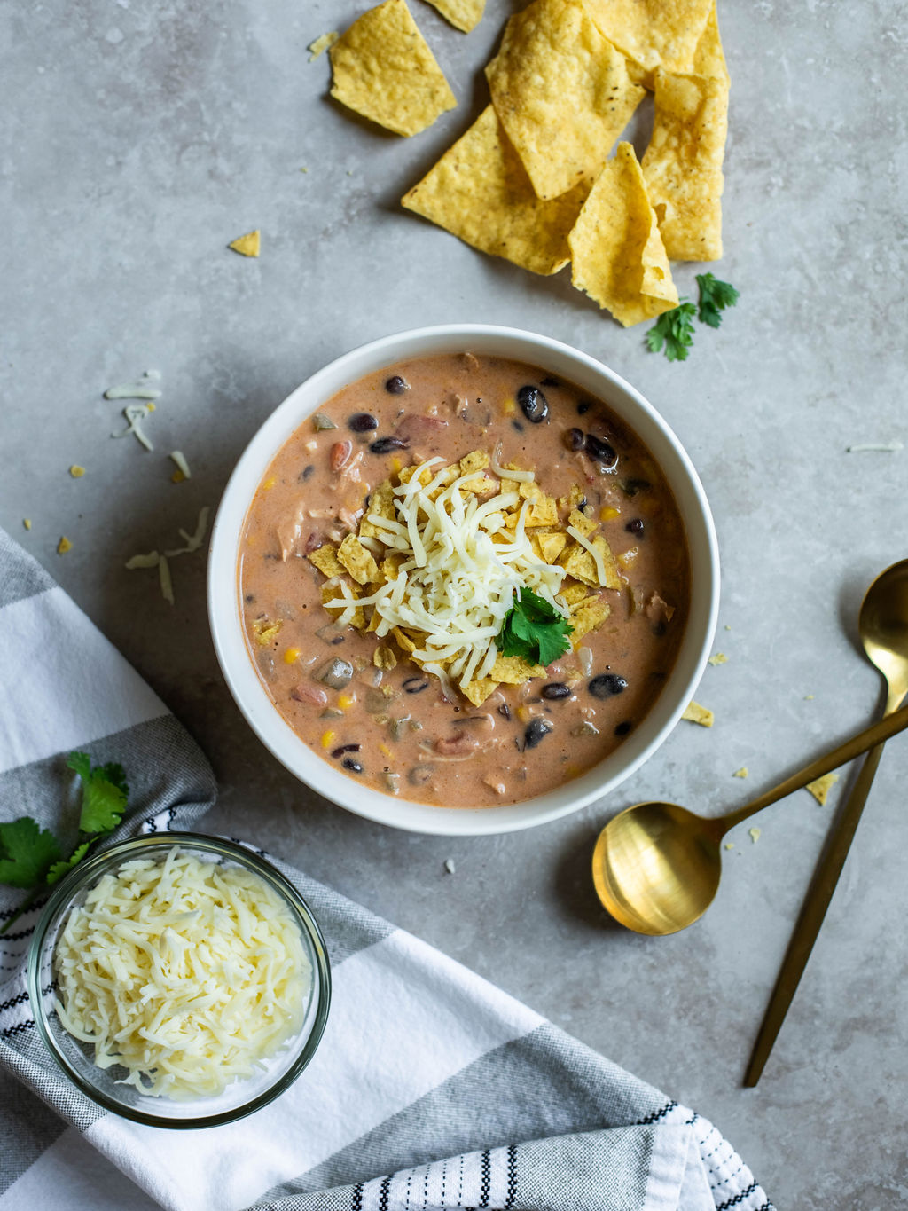 a bowl of cheesy chicken enchilada soup with cheese and crushed tortilla chips on top.