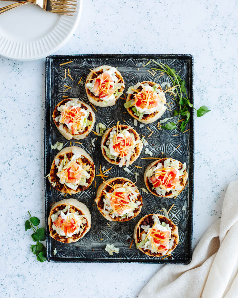 Taco Pinwheels topped with sour cream, tomatoes, and lettuce on a black board.