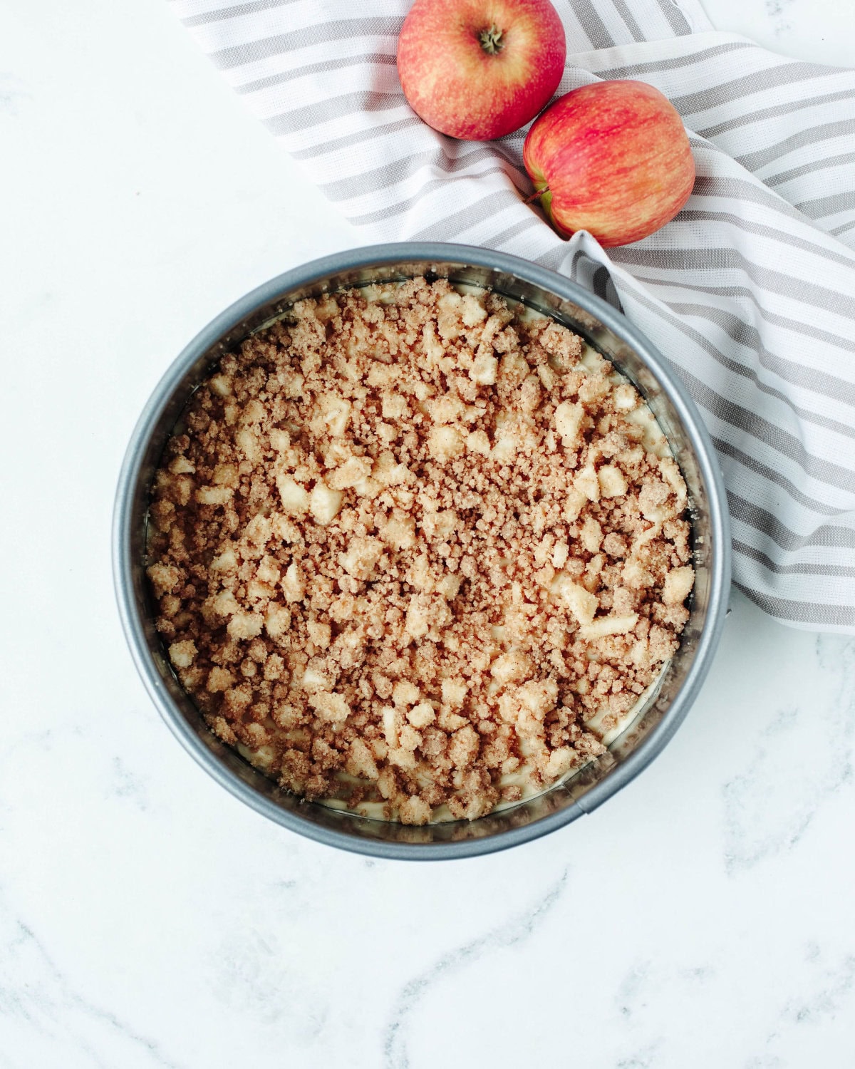 chopped apple and crumb topping sprinkled on top of cake batter in a springform pan.