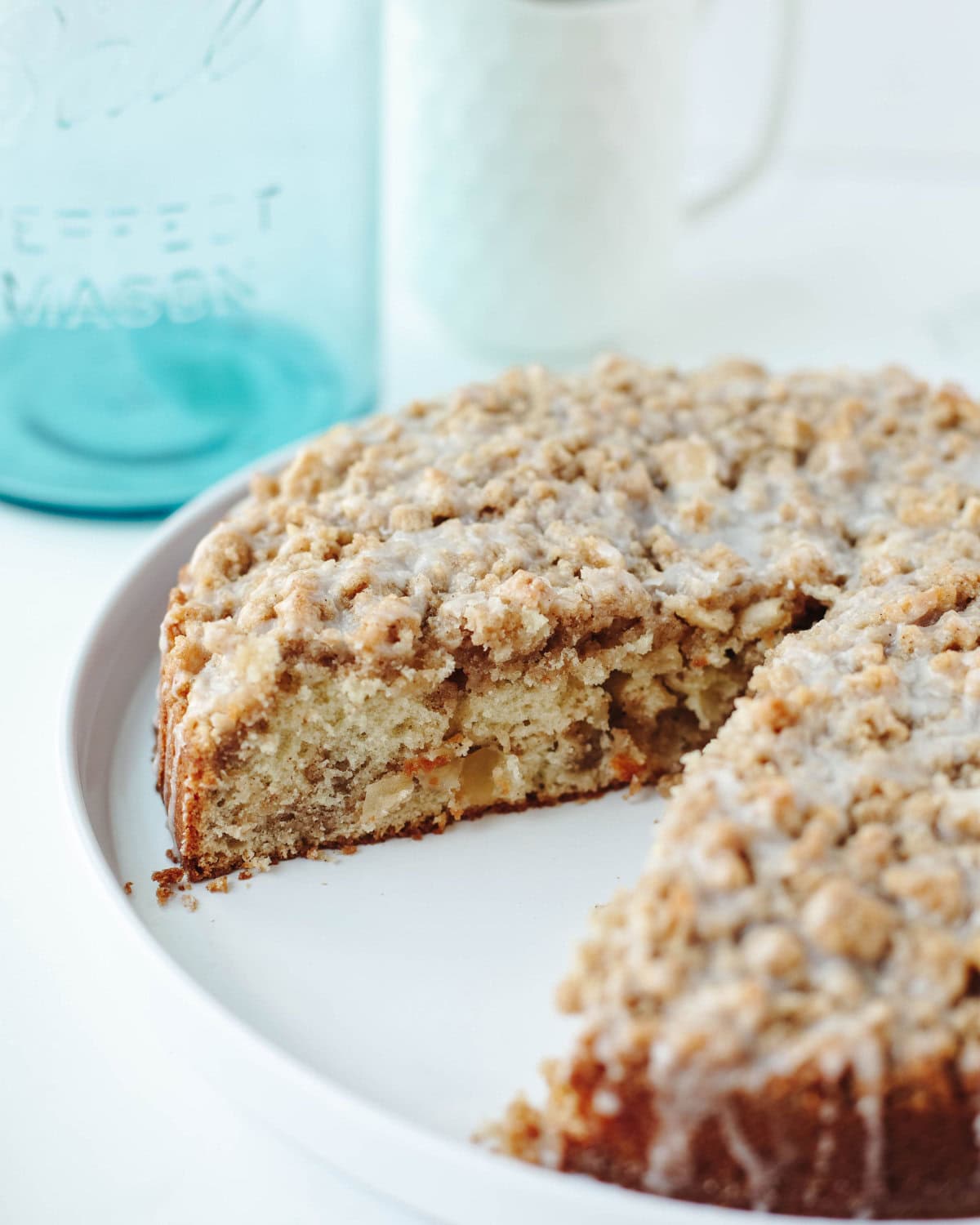 a slice taken out of a apple crumb cake on a white serving platter.