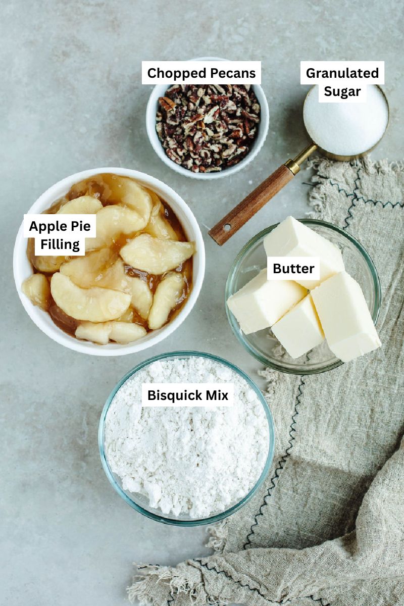 Ingredients for Bisquick apple cobbler including apple pie filling, Bisquick mix, sugar, butter, and chopped pecans.