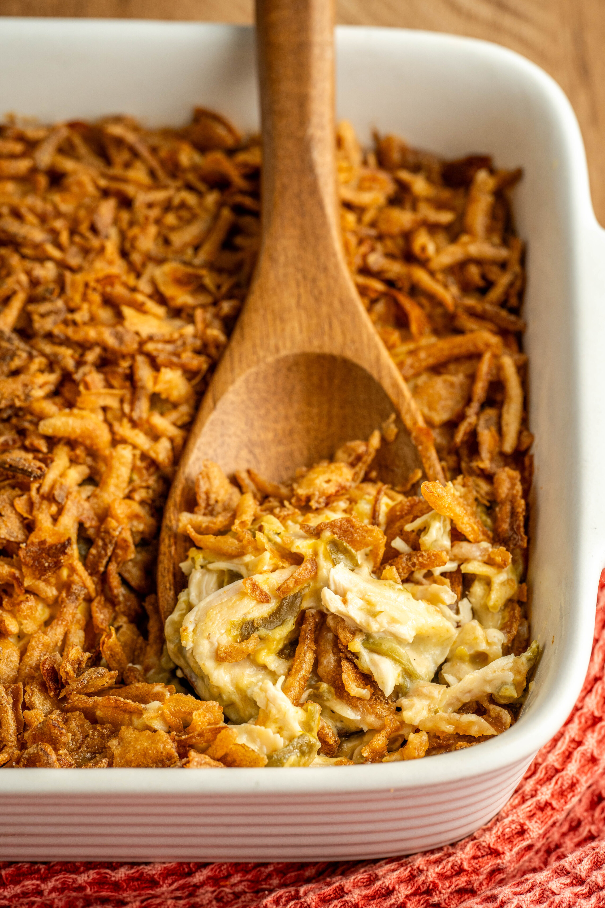 a wooden spoon scooping a serving of chicken casserole with French fried onions on top.