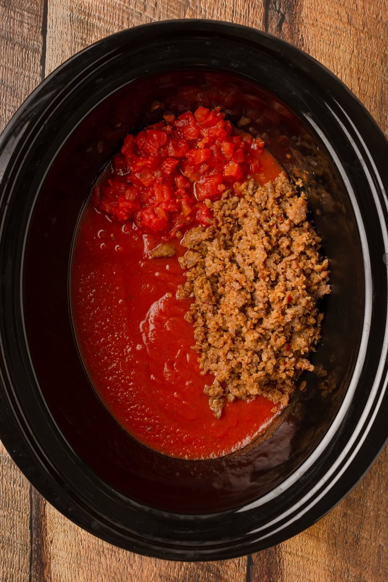 a crockpot with spaghetti sauce, diced tomatoes, and cooked Italian sausage.