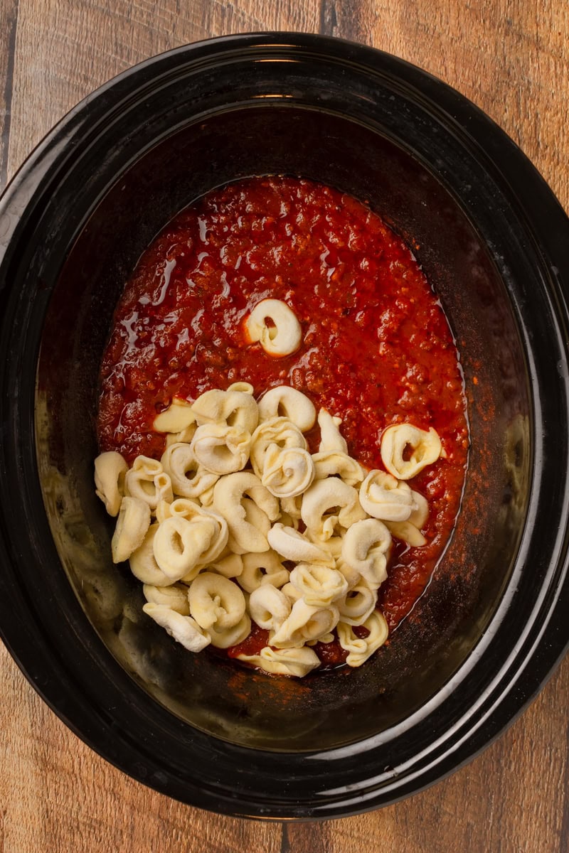 tortellini being added to spaghetti sauce in a crockpot.