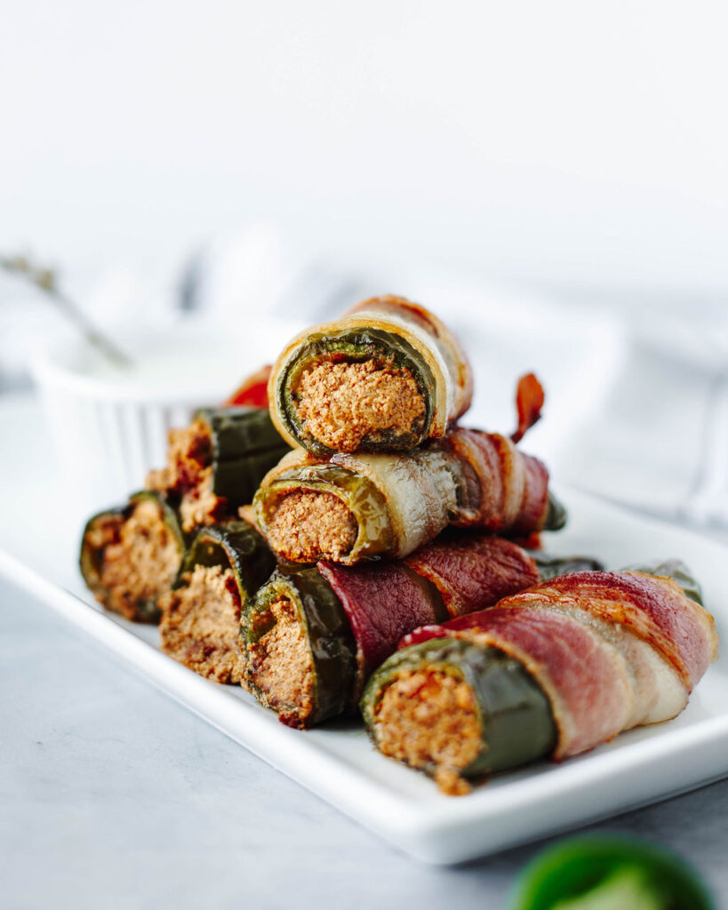 Stuffed Jalapenos cooked and stack on a white serving plate.