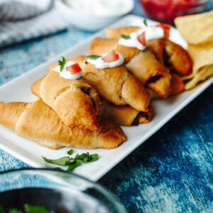 crescent taco rolls on a platter with sour cream and tomatoes.