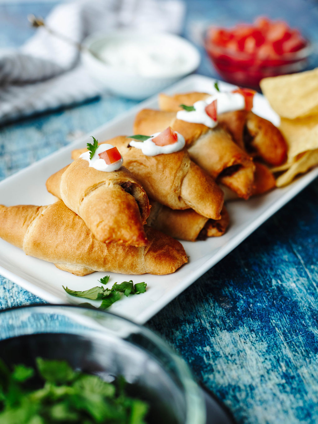 taco seasoned ground beef stuffed inside a crescent roll baked and served on a white plate.