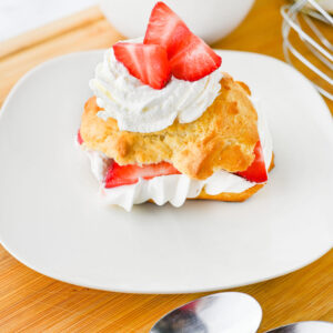 strawberry shortcake served on a white plate with whipped cream.