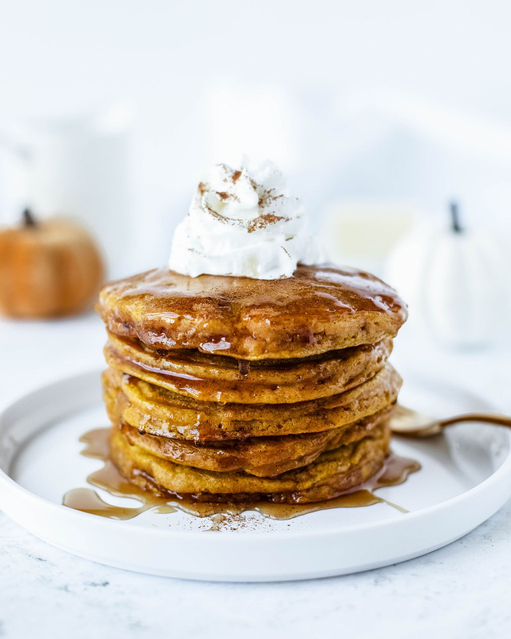 pumpkin pie spice pancakes on a white plate with whipped cream and syrup.