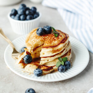 a bite of pancakes on a fork next to a stack with syrup.
