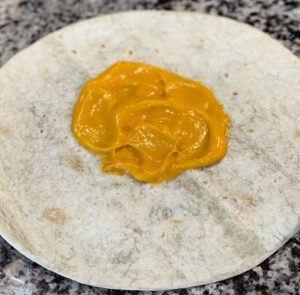 nacho cheese spread on a flour tortilla