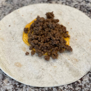 seasoned taco beef over nacho cheese on a flour tortilla