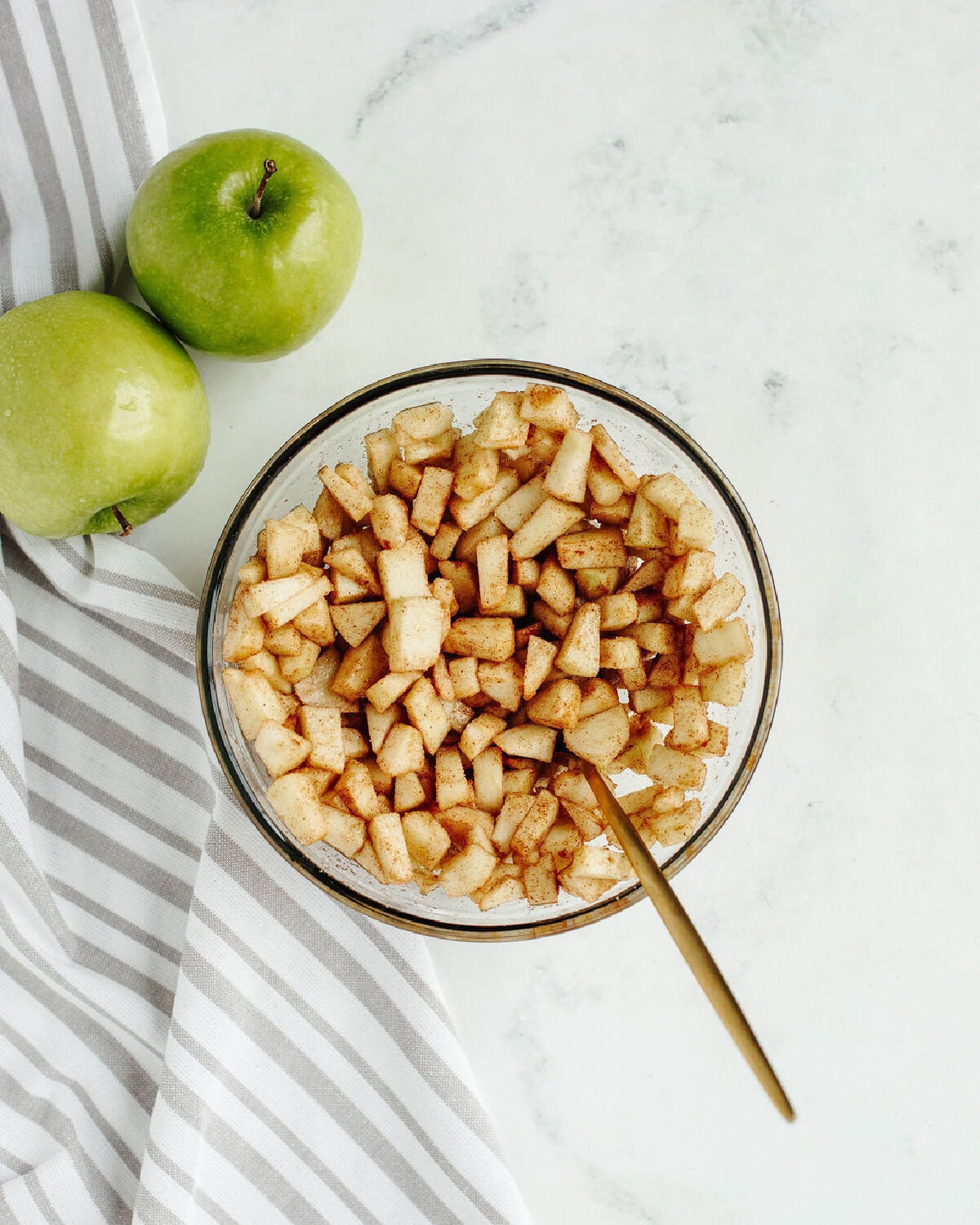 chopped apples combined with cinnamon and sugar in a glass bowl.