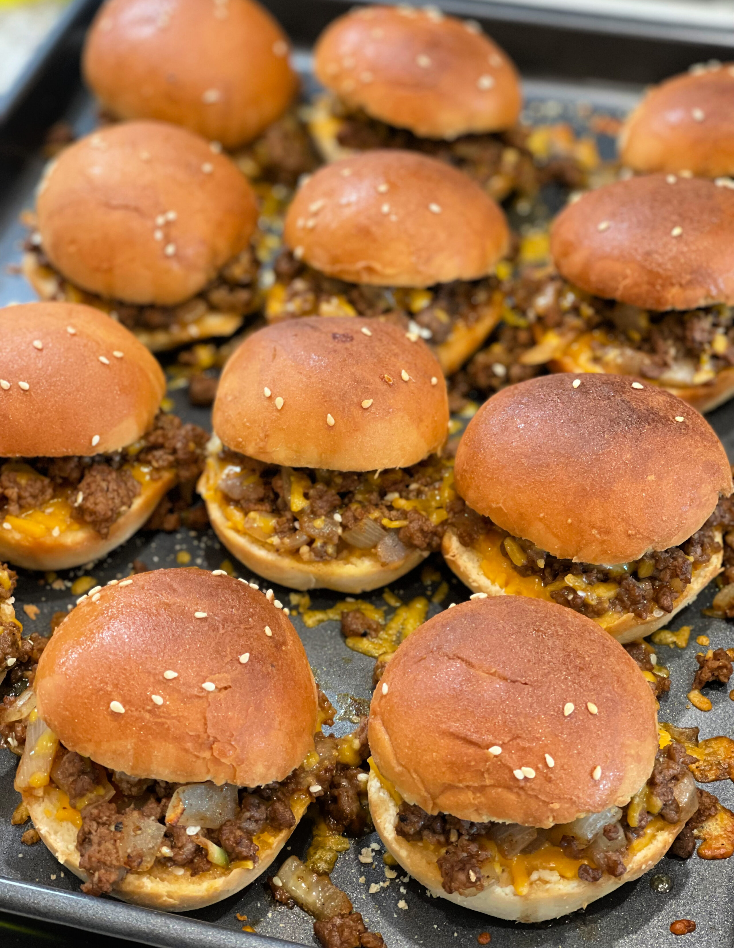 sloppy joe sliders lined up on a cookie sheet after baking in the oven.