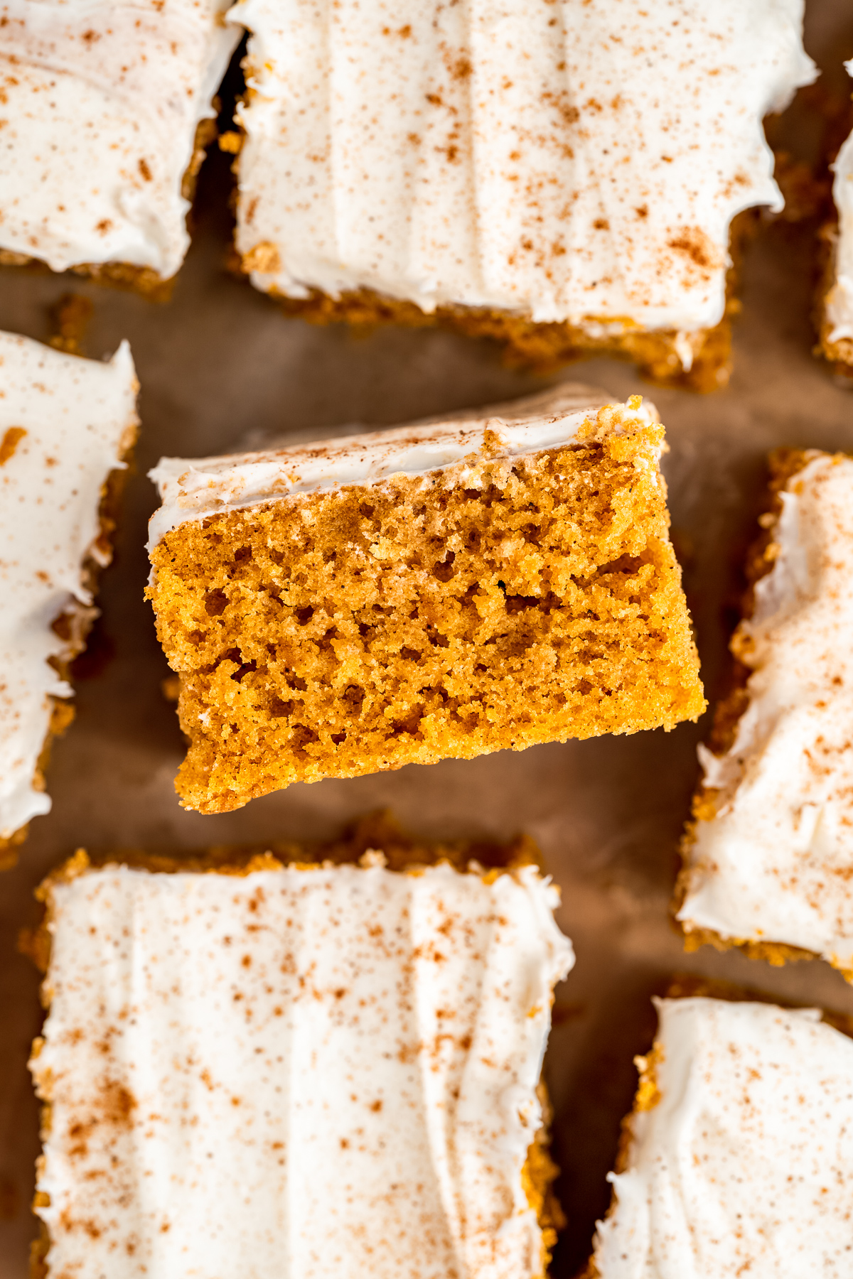 pumpkin bars with cream cheese frosting sliced on parchment paper.