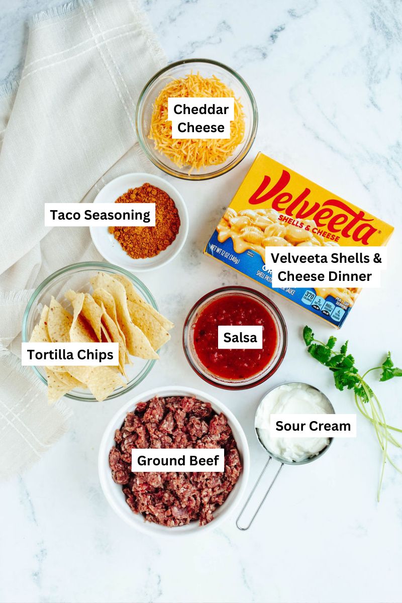 Ingredients for nacho bake recipe including pasta, ground beef, Velveeta shells and cheese, salsa, and tortilla chips.