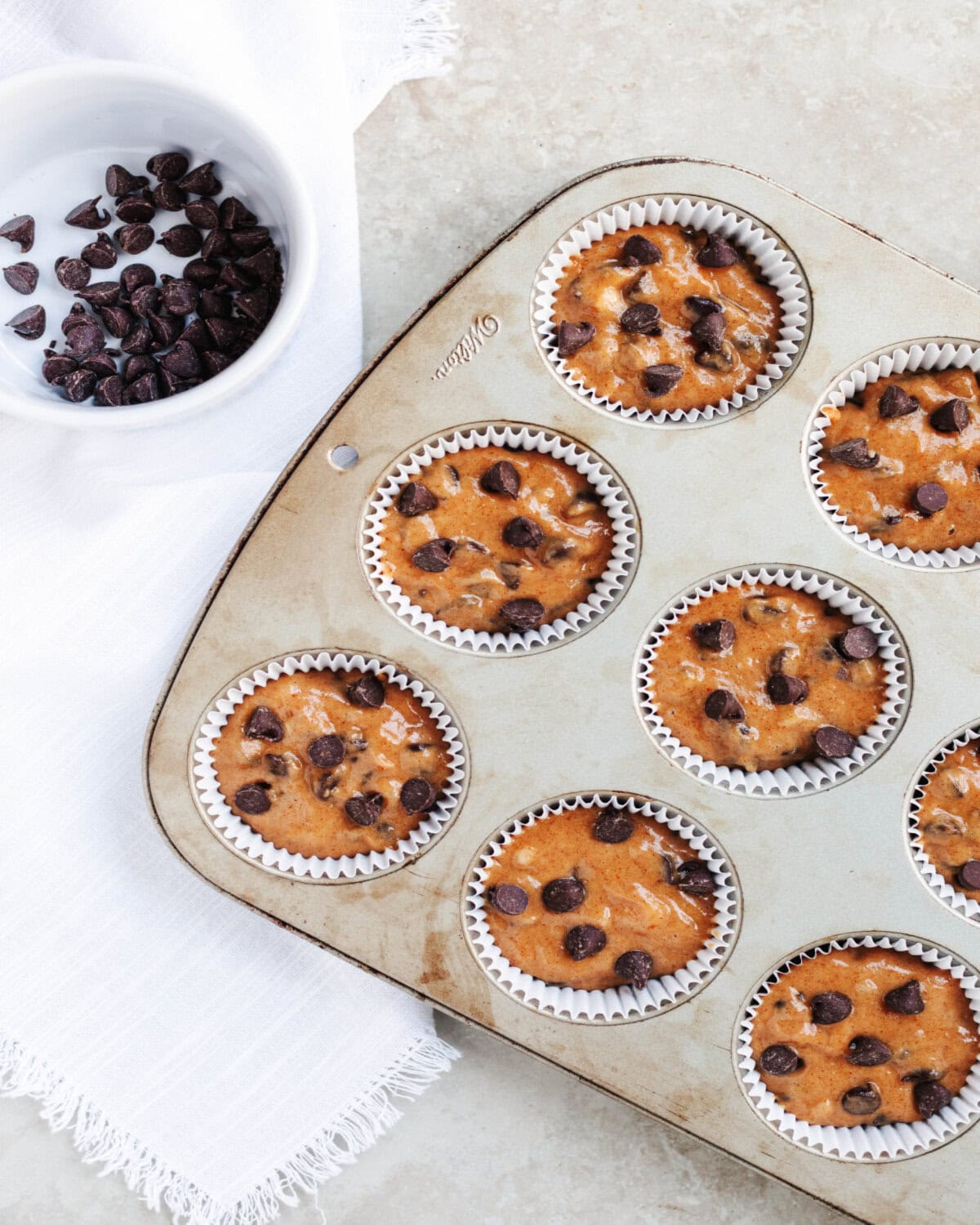 A paper-lined muffin tray filled ¾ full with pumpkin banana muffin batter.
