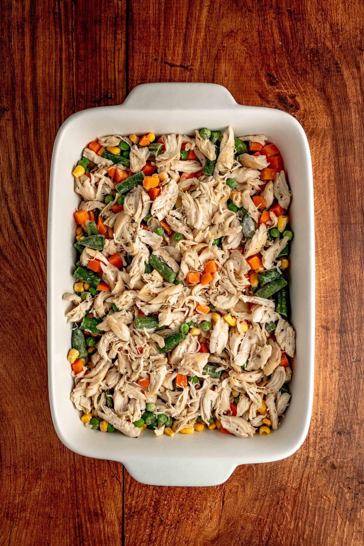 shredded chicken and frozen vegetables in a casserole pan.