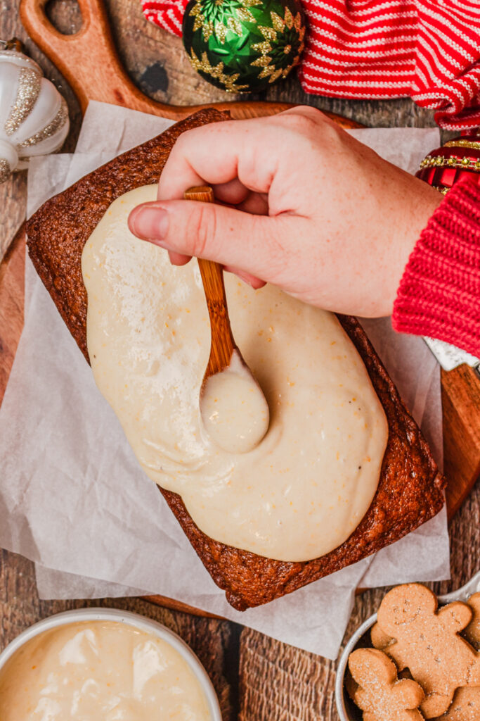 pouring homemade cream cheese frosting over a warm quick bread.